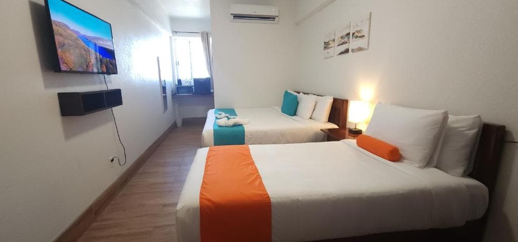 A well-lit hotel room featuring two beds, a television mounted on the wall, and colorful bedding.