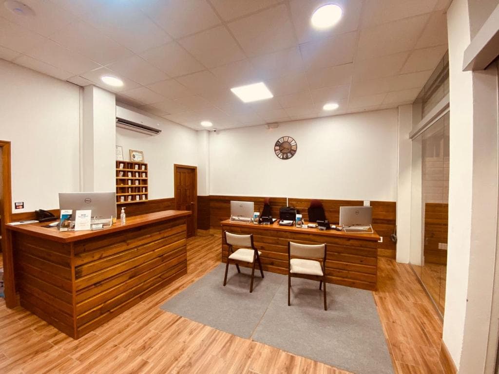 A modern office reception area featuring wooden accents, two chairs, and computers on a desk.
