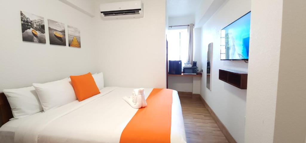A cozy hotel room featuring a double bed with orange accents, a television, and artwork on the walls.