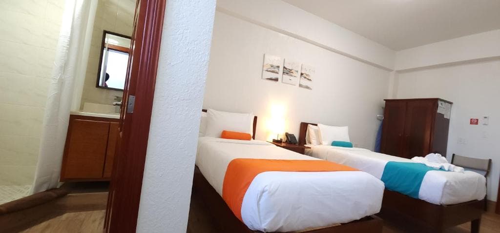 A hotel room featuring two beds with colorful accents and a bathroom in view.