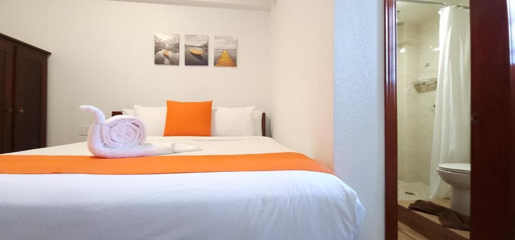 A cozy hotel room featuring a neatly made bed with an orange accent, decorative wall art, and an en-suite bathroom.