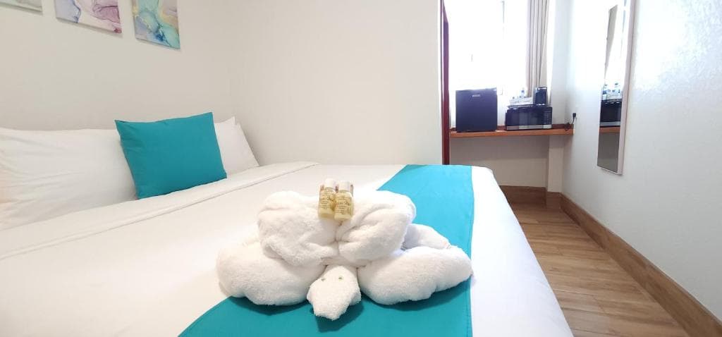 A neatly made bed with turquoise accents and a decorative arrangement of white towels resembling a swan.