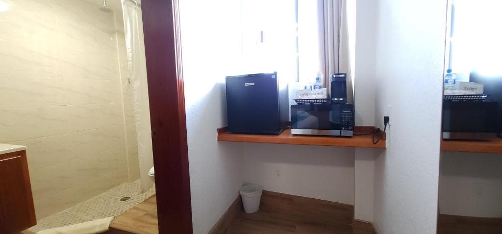 A small kitchen area featuring a refrigerator and microwave next to a bathroom with a shower.