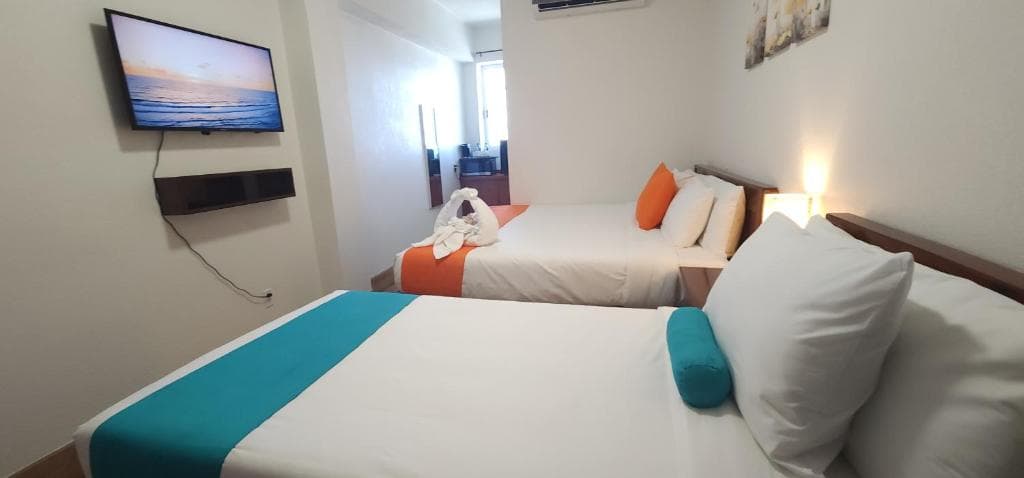 A cozy hotel room featuring two beds, a wall-mounted TV, and colorful accents.