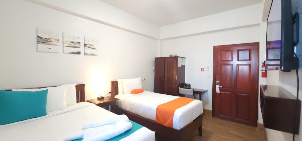A simple hotel room featuring two beds, a wooden wardrobe, and a TV on the wall.