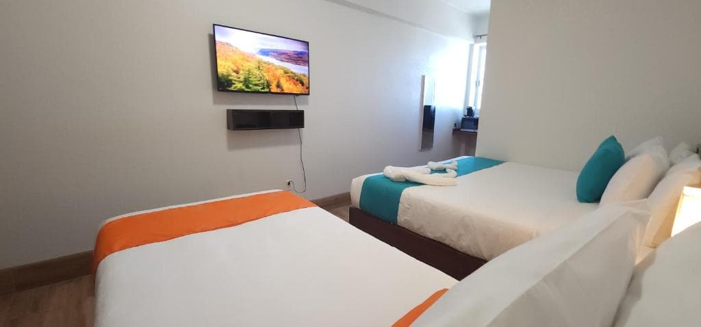 A modern hotel room featuring two beds, a TV, and blue and orange accents.
