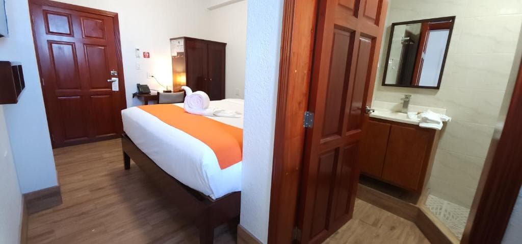 A hotel room featuring a bed with an orange accent, a desk, and an attached bathroom.