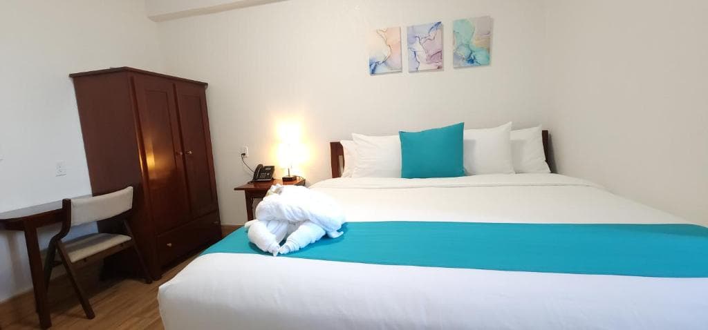 A cozy hotel room featuring a large bed with a turquoise accent, a wooden wardrobe, and abstract wall art.