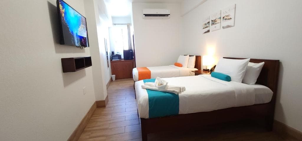 A modern hotel room featuring two beds, a TV, and a bright interior.