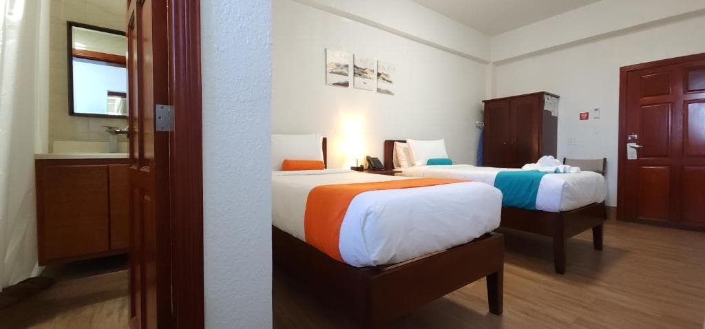 A hotel room featuring two twin beds with colorful accents and a small bathroom area visible.