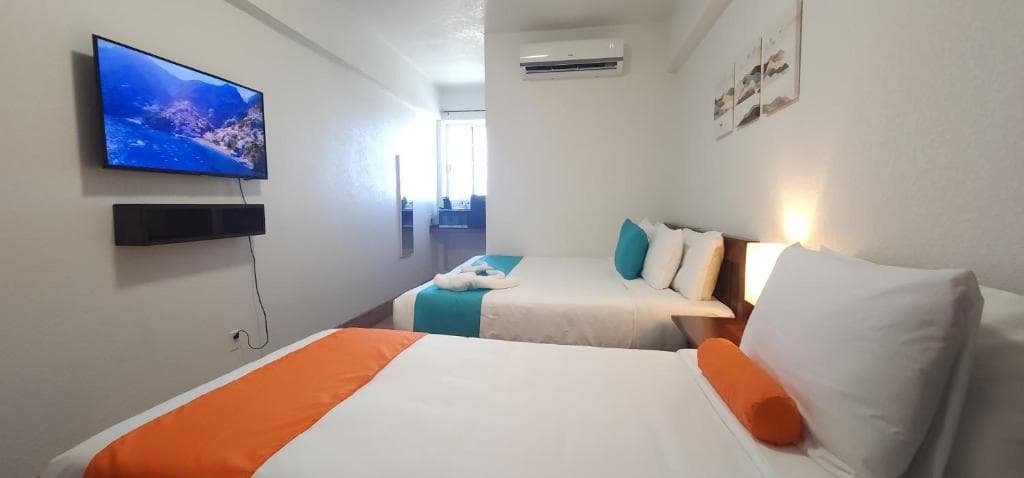 A modern hotel room featuring two beds, a wall-mounted TV, and bright décor.